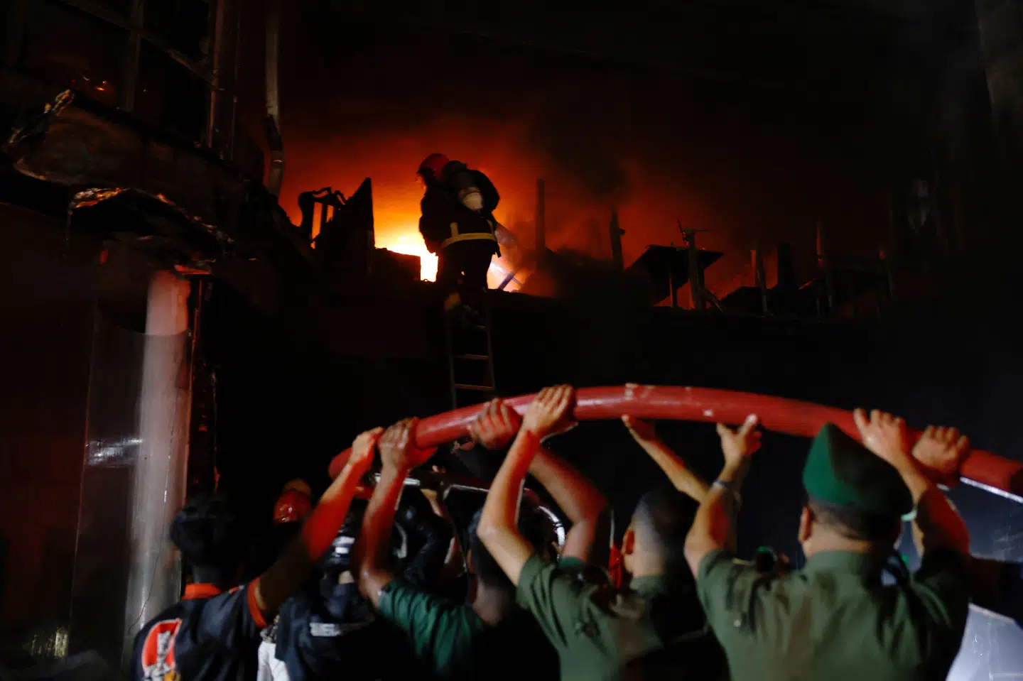 Frivillige bærer på en vandslange, mens en brandmand er i gang med at slukke ilden i den etagebygning i Dhaka, hvor mindst 43 mennesker har mistet livet i en brand.