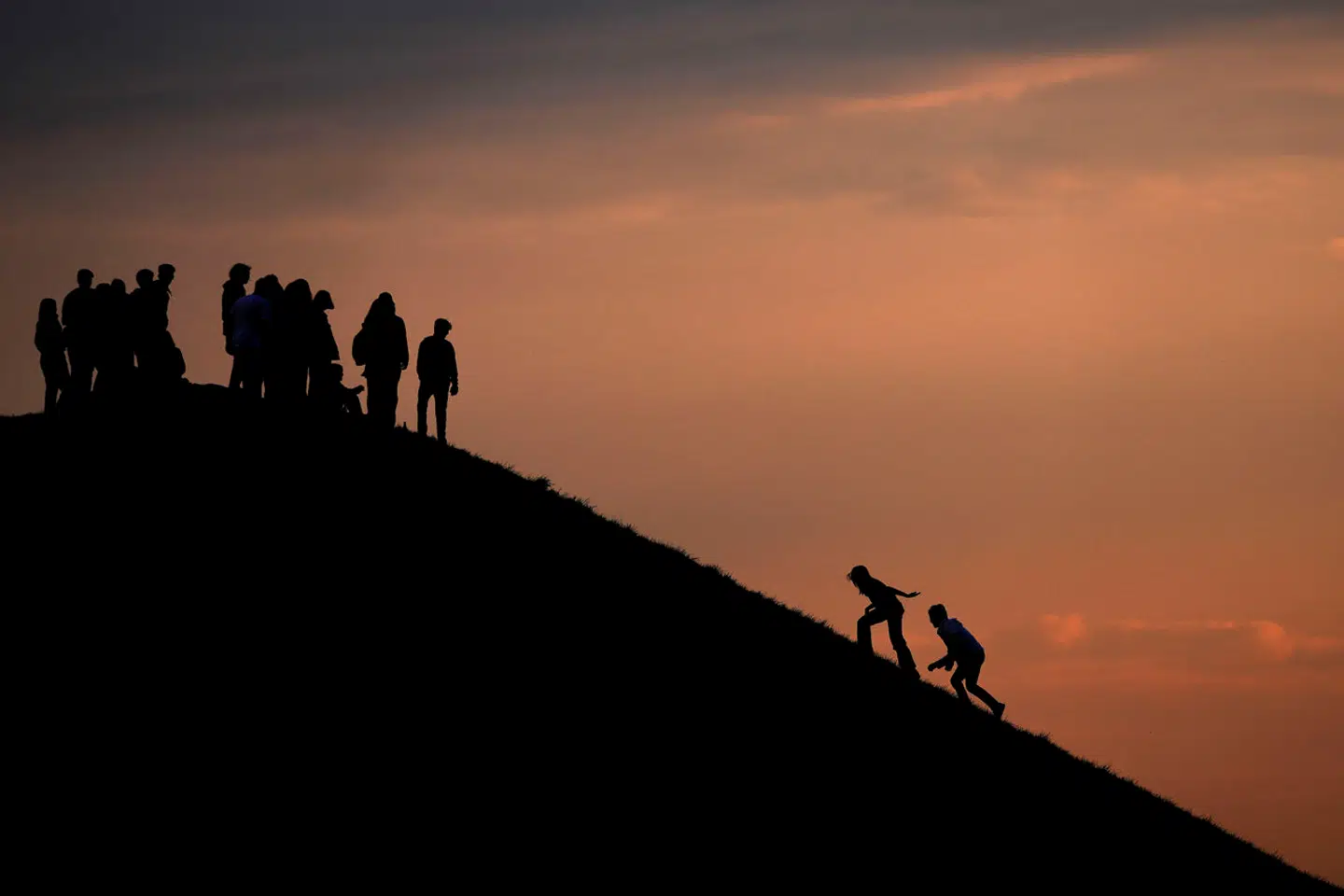 A couple climb up a hill while people enjoy the sunset at the Olympic park in Munich, Germany, Monday, May 2, 2022. (AP Photo/Matthias Schrader)