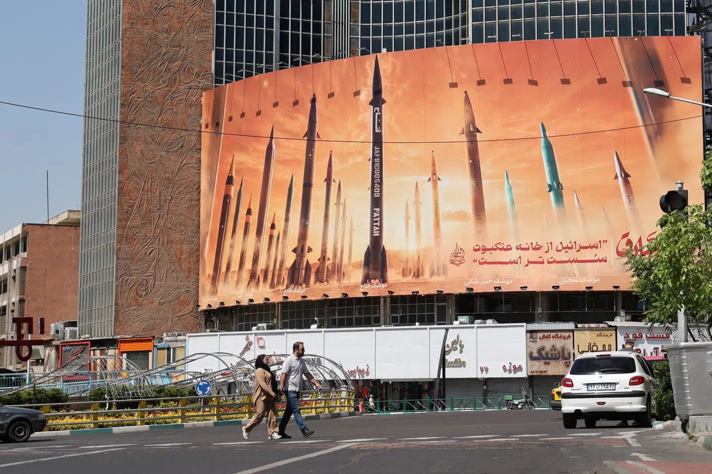 På gaden i Teheran går to mennesker fredag foran en stor antiisraelsk plakat med et billede af iranske missiler.