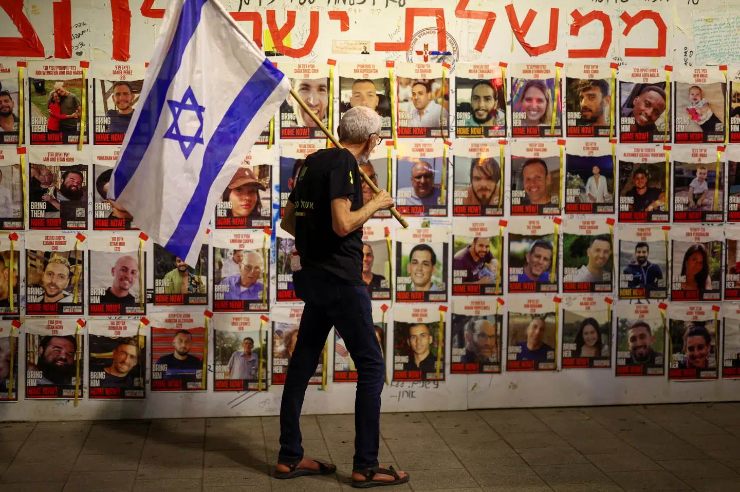 En mand bærer et israelsk flag under en demonstration i Tel Aviv tidligere i april. Han står foran en væg med billeder af israelske gidsler, der endnu sidder fanget i Gaza. (Arkivfoto).