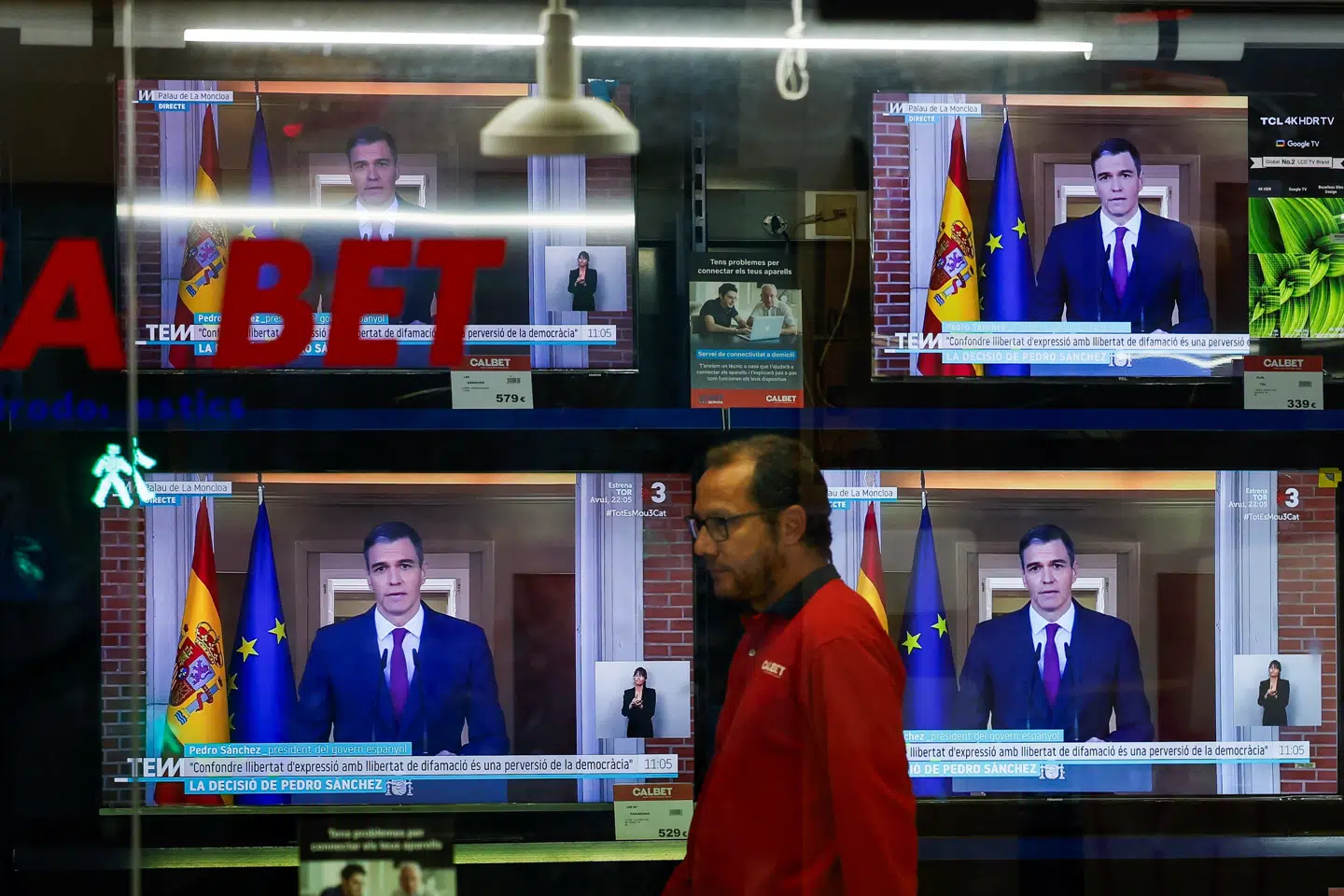 En person i Madrid går forbi tv-skærme, der viser Spaniens premierminister, mens han mandag meddeler, at han har besluttet sig for at fortsætte som regeringsleder.