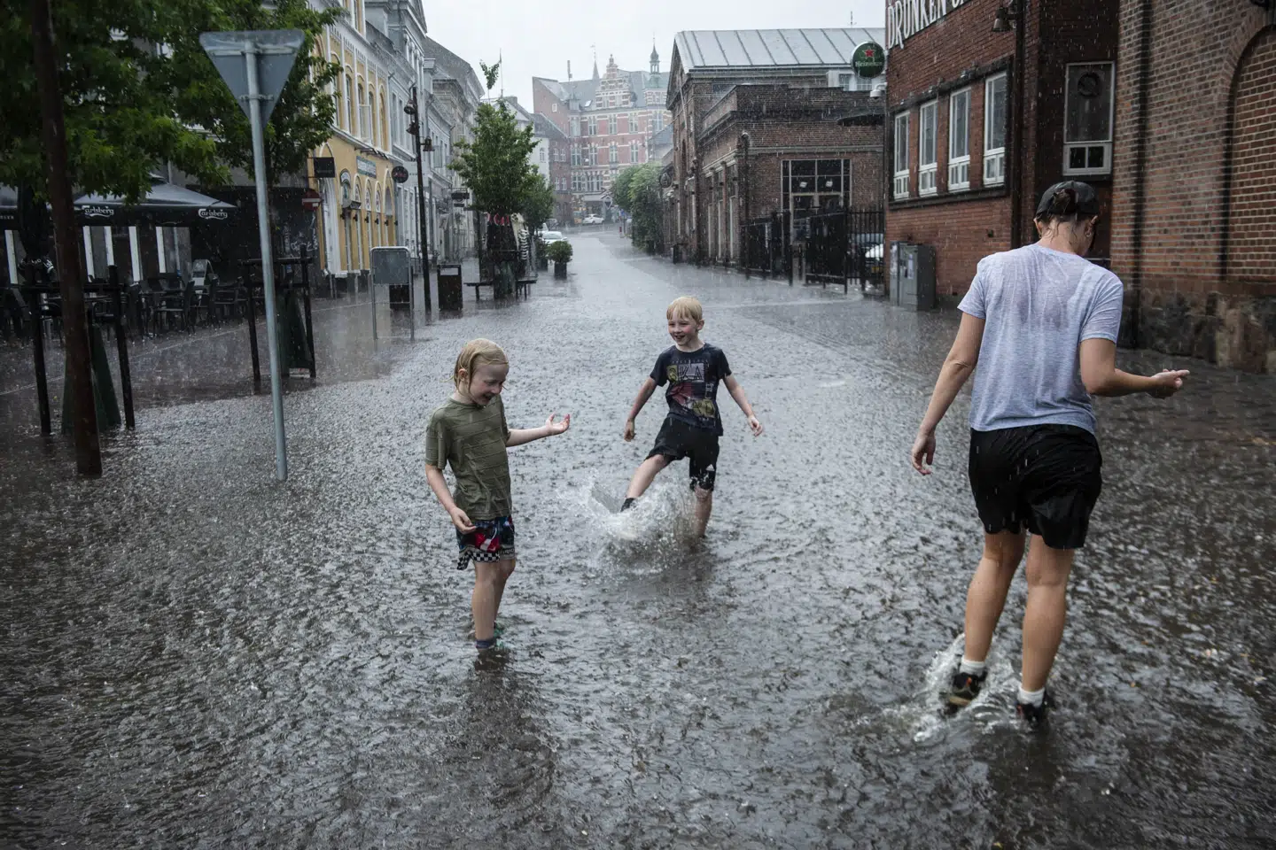 Drenge i regnen på den oversvømmede Frederiksgade i Svendborg på Fyn, mandag den 26. juni 2023. Denne weekend byder på risiko for kraftige byger, hvor der falder mere end 15 millimeter på 30 minutter. (Arkivfoto).