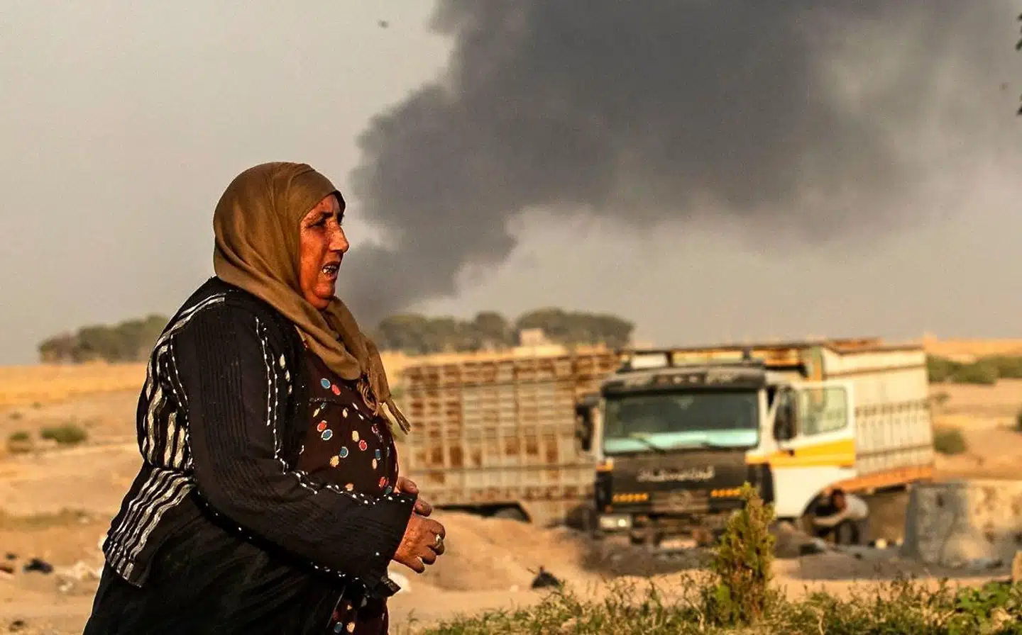 En kurdisk kvinde ser til, mens røgen stiger til vejrs fra tyrkiske bombardementer inde i det kurdiske område i Syrien.