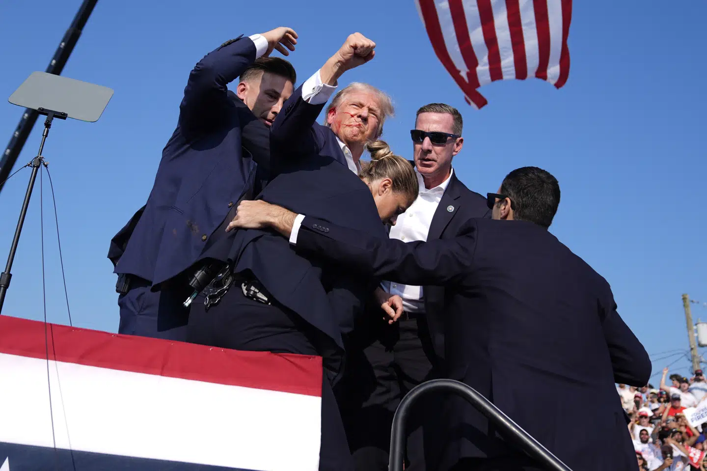 På billeder og videooptagelser kan man se, at Donald Trump løfter en knytnæve i vejret efter meldinger om skud.