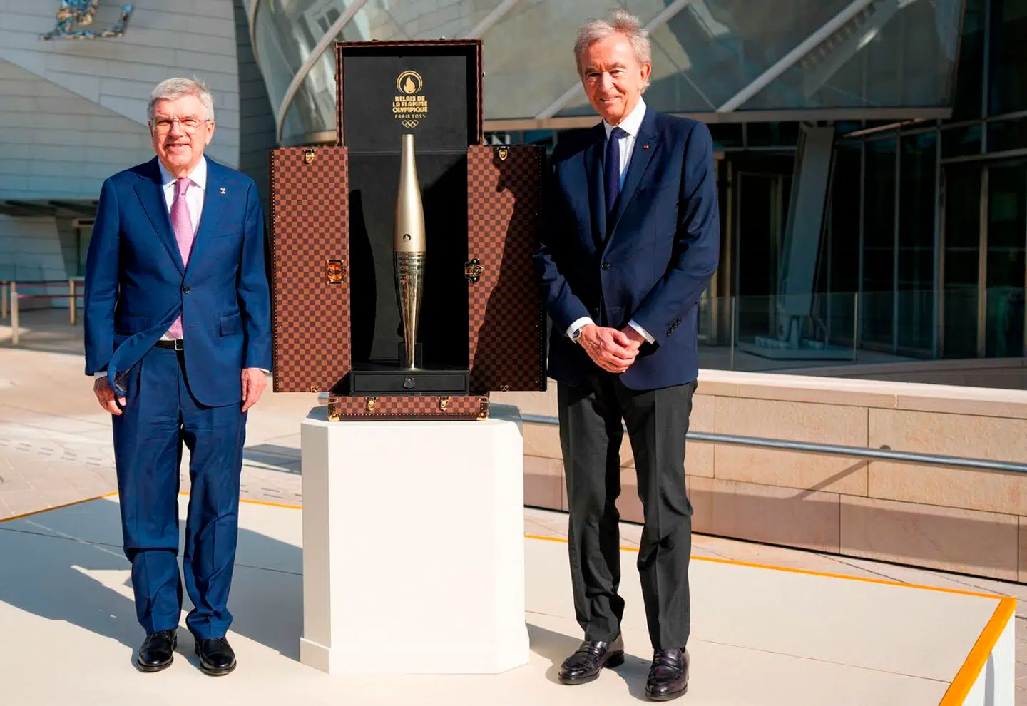 Den franske rigmand Bernard Arnault (th.) smilede stort, da han i Paris i denne uge fremviste en særlig kuffert med den olympiske fakkel, designet af hans luksusvaremærke Louis Vuitton, forud for åbningen af De Olympiske Lege i Paris. Den Internationale Olympiske Komités formand, Thomas Bach, flankerer faklen.