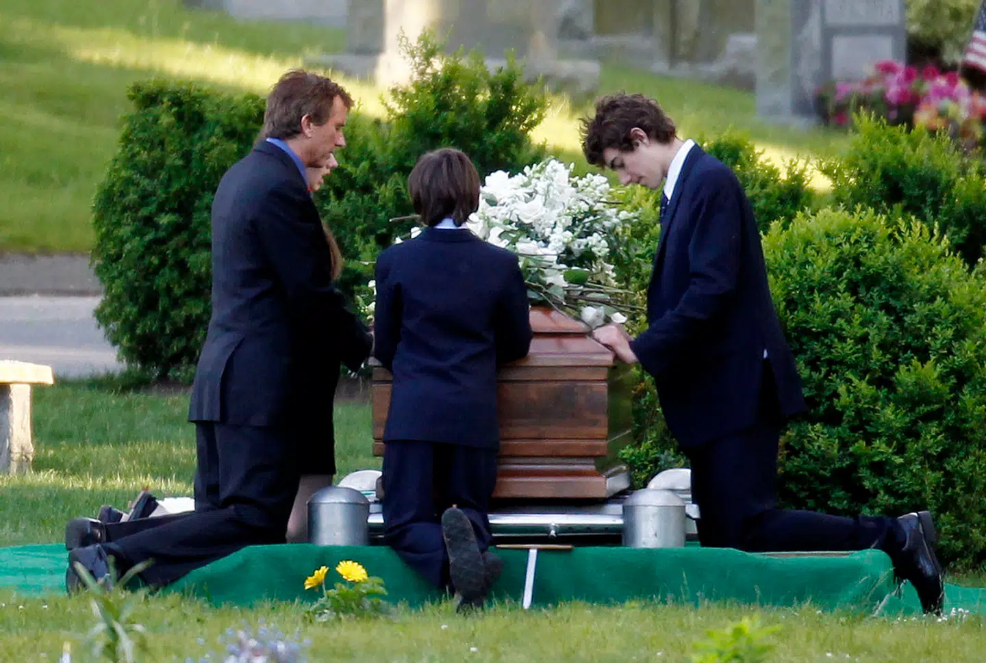 Virkeligheden, som Kennedy-familien gerne ville have den til at se ud – Robert F. Kennedy Jr. (tv.) knæler ved siden af kisten med sin afdøde kone, som han støttede gennem hendes ulykke. Ved siden af er parrets børn. Virkeligheden var en helt anden, og selv gravstedet var fup.