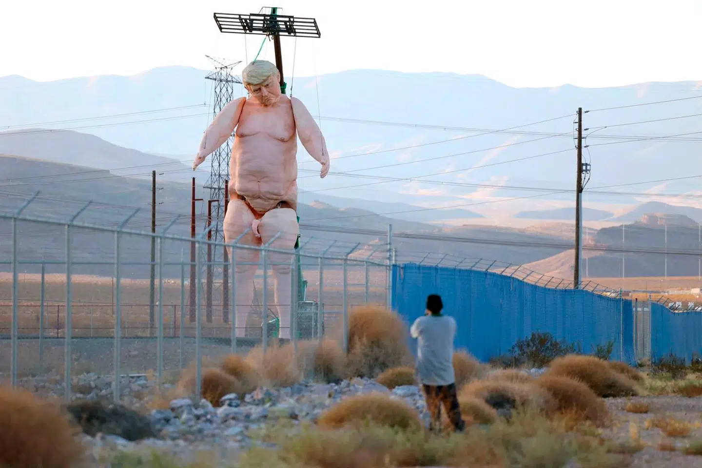 TOPSHOT - A man takes a photo of a 43-foot-tall (13 meters) naked statue resembling former US President and Republican presidential candidate Donald Trump displayed in a fenced-in lot near Interstate 15 north of Las Vegas, Nevada, September 28, 2024. Made of foam over rebar and weighing approximately 6, 000 pounds (2722 kilos), the gigantic display will will criss-cross the US as part of the "Crooked and Obscene Tour." (Photo by Ronda Churchill / AFP)