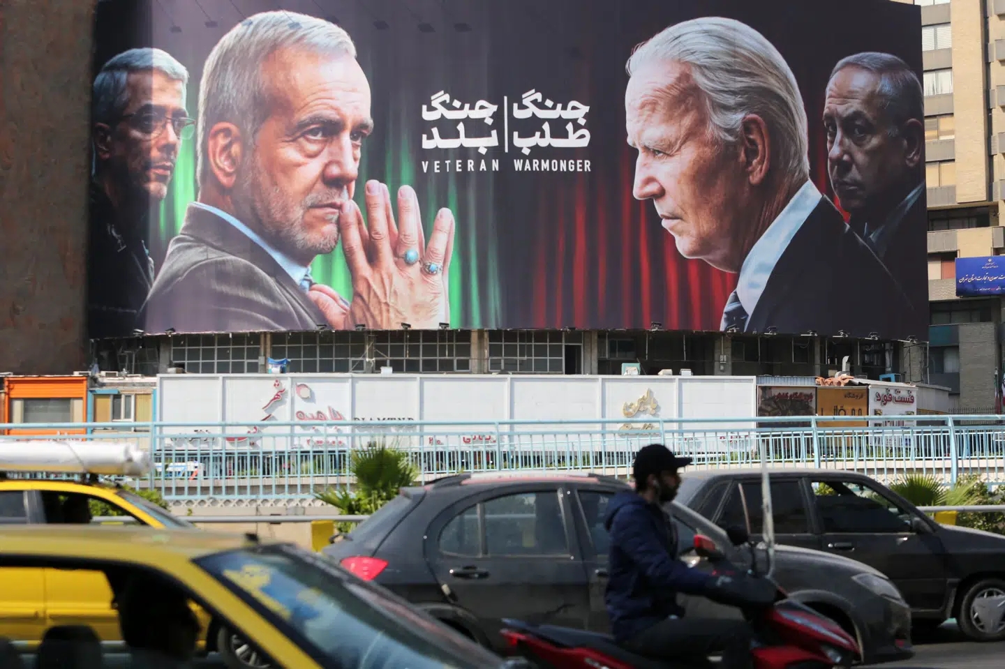 Pendlere i Teheran kører forbi en plakat med billeder af Irans præsident, Masoud Pezeshkian, hærchef Mohammad Bagheri, præsident for USA Joe Biden og den israelske premierminister, Benjamin Netanyahu. Billedet er taget dagen efter israelske luftangreb i Iran.