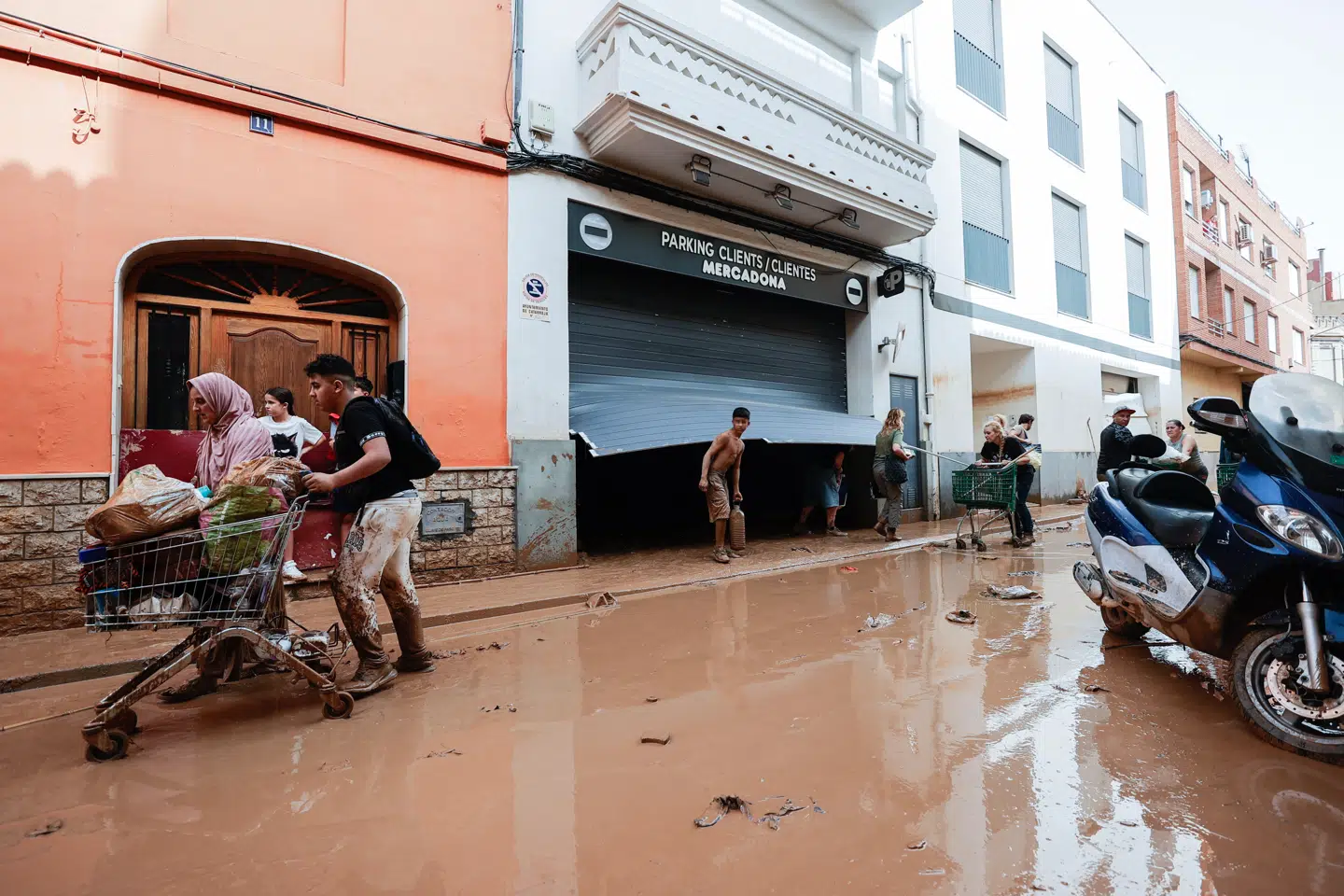 Indbyggere tager ting fra et supermarked i Valencia og går derfra gennem de stadigt mudrede og våde gader.