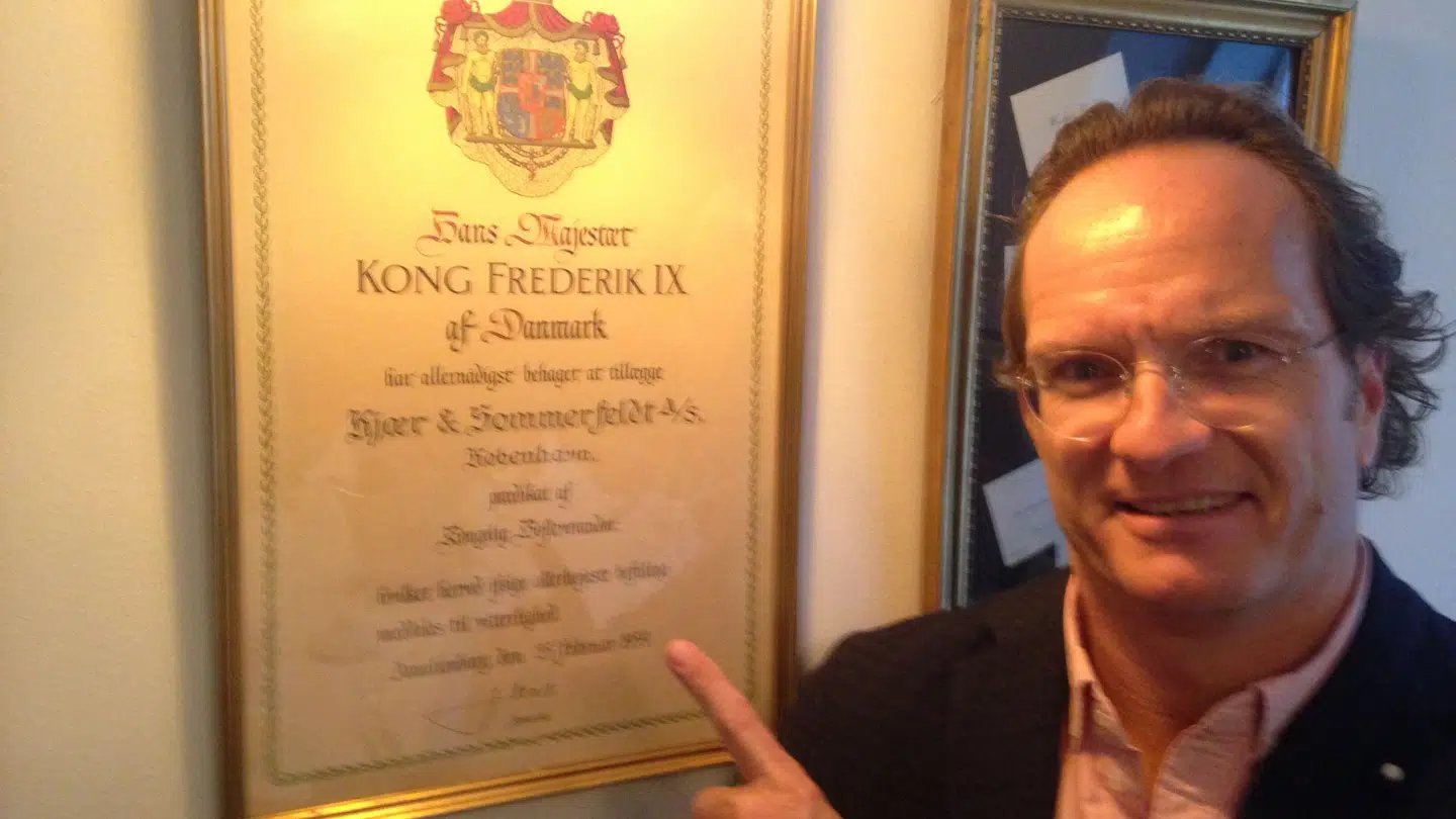 Kjær & Sommerfeldts administrerende direktør og ejer, den tidligere VM-spiller i ishockey Mads Stensgaard, med diplomet med teksten: Hans Majestæt Kong Frederik IX af Danmark har allernådigst behaget at tillægge Kjær & Sommerfeldt A/S, København, prædikat af Kongelig Hofleverandør.