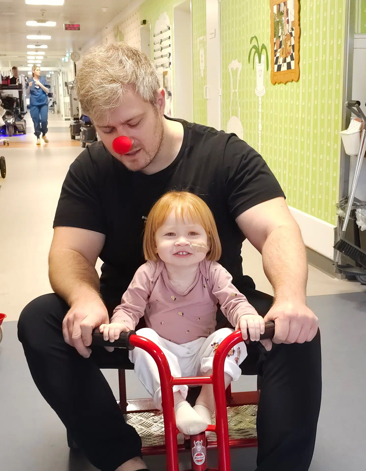 Mille cykler med far, som har en klovnenæse på. Den har han fået af hospitalsklovnene.