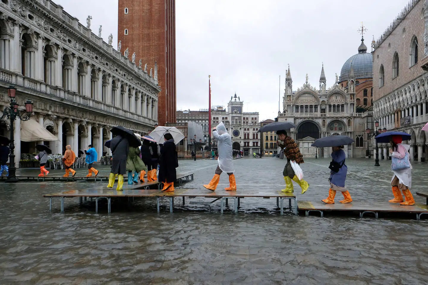 Folk går på gangbroer hen over Markuspladsen i Venedig.