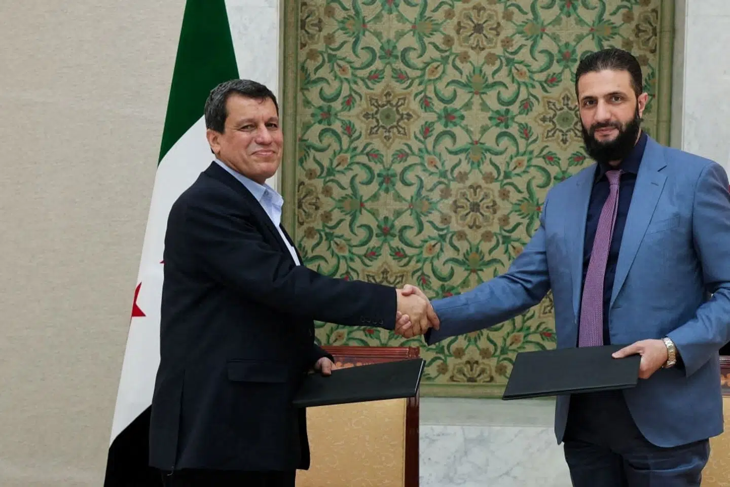 Syriens midlertidige præsident, Ahmed al-Sharaa (til højre), og SDF-leder Mazloum Abdi giver hinanden hånden, efter at de begge har underskrevet aftale om integrere SDF-institutioner i den syriske stat.