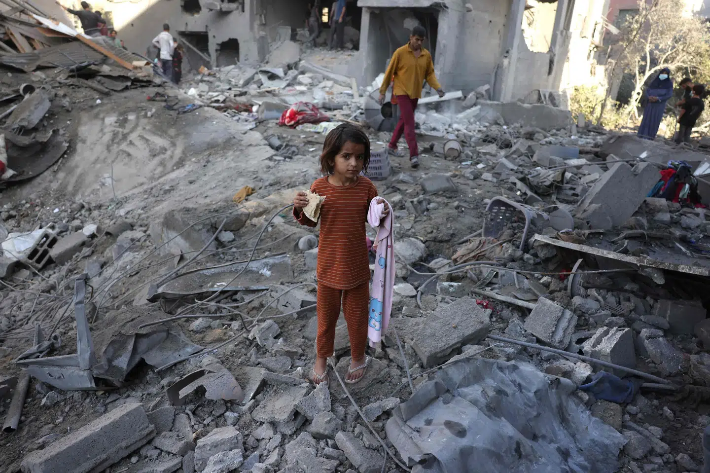 En pige spiser en skive brød, mens andre palæstinensere omkring hende besigtiger skaderne efter et nyt israelsk angreb i Jabalia i den centrale del af Gazastriben fredag. Israel advarer om en endnu hårdere kurs, hvis Hamas ikke accepterer et amerikansk forslag om våbenhvile og frigivelse af gidsler.