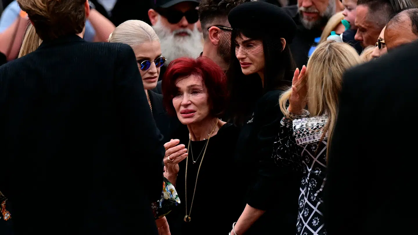 Her står Sharon Osbourne omringet af sine to døtre ved sin mands mindeoptog.