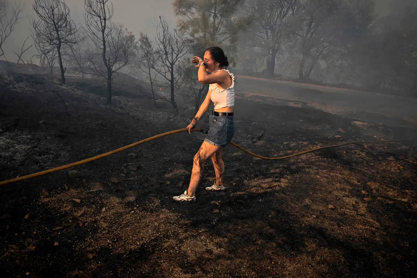 En kvinde forsøger at slukke gløder efter naturbrand i det nordvestlige Spanien, der har været ramt af usædvanligt mange brande i år.