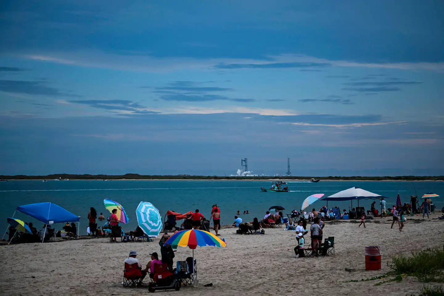 Folk sidder klar på South Padre Island i Texas, mens SpaceXs Starship-raket øjnes i baggrunden. SpaceX aflyste dog den planlagte testflyvning søndag blot 30 minutter før opsendelsen – som seneste tilbageslag for Elon Musk, der ejer selskabet.