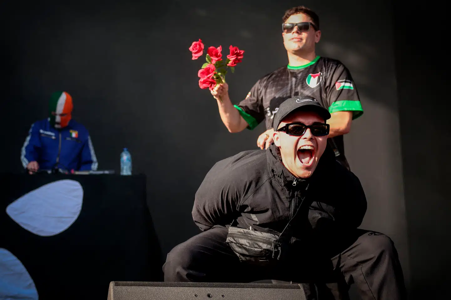 Liam Óg Ó hAnnaidh (forrest) optræder under navnet Mo Chara, Naoise O Caireallain (med blomster i hånden) optræder under navnet Moglai Bap, og J.J. O Dochartaigh, som optræder under navnet DJ Provai, står bagerst ved dj-pulten.