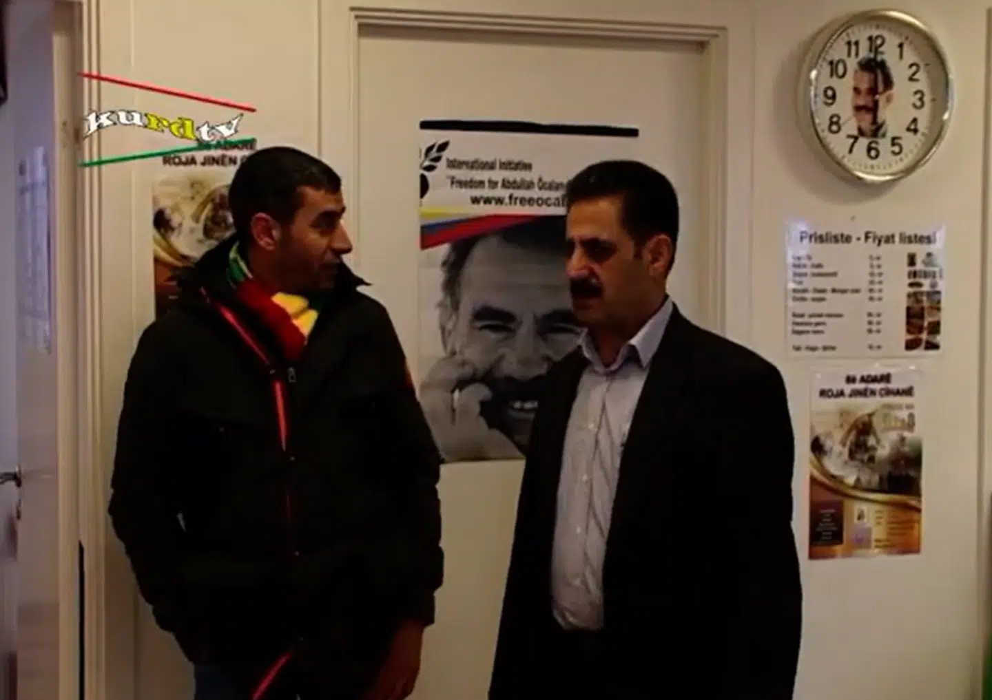 Her ses to deltagere til mindehøjtideligheden. Bag dem er en plakat samt et vægur med billeder af den fængslede grundlægger og leder af PKK, Abdullah Öcalan.