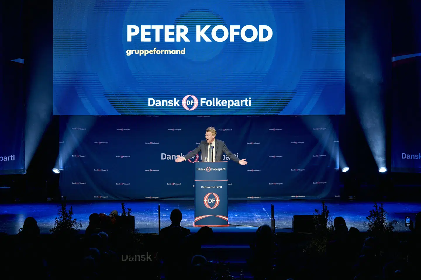 Da årsmødet indledes klokken 12, bliver lyset slukket over de flere hundrede delegerede, mens en dramatisk videopræsentation tændes på tre skærme, hvorefter Peter Kofod indtager scenen.