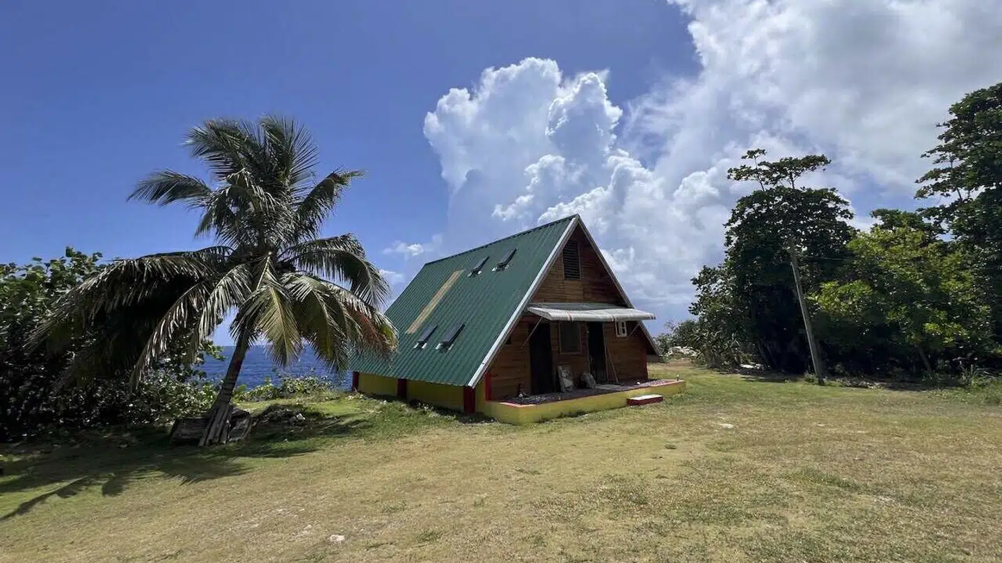 Joan Vedel hjælper sin mand med at drive et bed and breakfast. Det er denne hytte, som hun opholder sig i, når hun er i Jamaica. De er evakueret fra hytten under orkanen, da den ligger for tæt på havet.