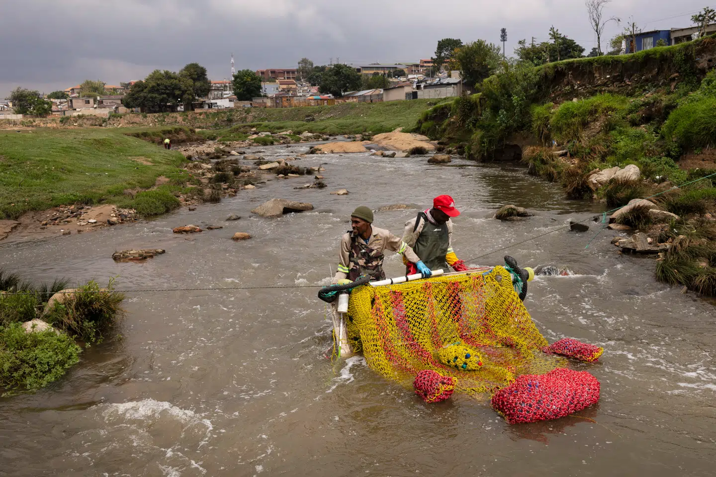 To frivillige fra Alexandra Township Water Warriors hjælper med at placere en affaldsfælde for at rense Jukskei-floden, der løber gennem Johannesburg, Sydafrika. Alexandra Township er en af byens fattige byområder og er plaget af uindsamlet affald og beskidt spildevand.