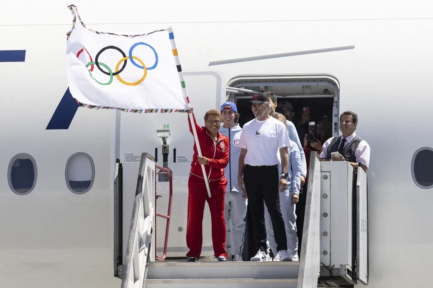 Karen Bass vifter i 2024 med det olympiske flag, mens Casey Wasserman i hvid t-shirt ser til. (Arkivfoto).