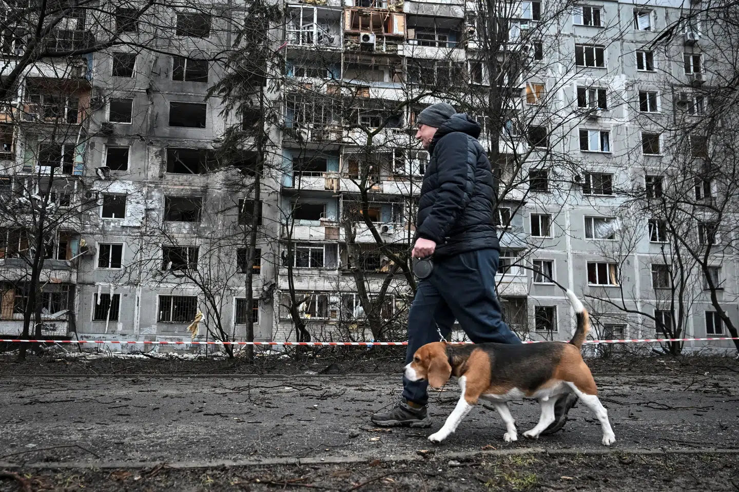 En mand lufter sin hund uden for en beboelsesejendom i Zaporizjzja, som natten til torsdag er blevet ramt i et af de russiske angreb.
