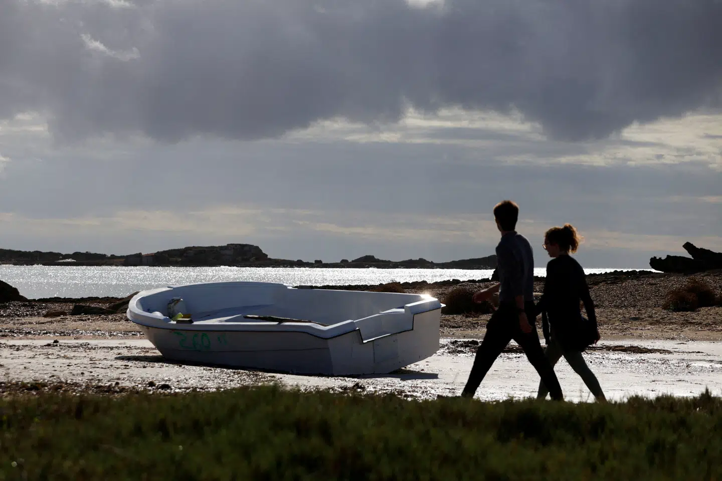 Folk går på Mallorca i nærhed af en båd brugt af migranter til at nå den spanske ø. Mange migranter søger mod netop Spanien i håbet om at komme til Europa. (Arkivfoto).