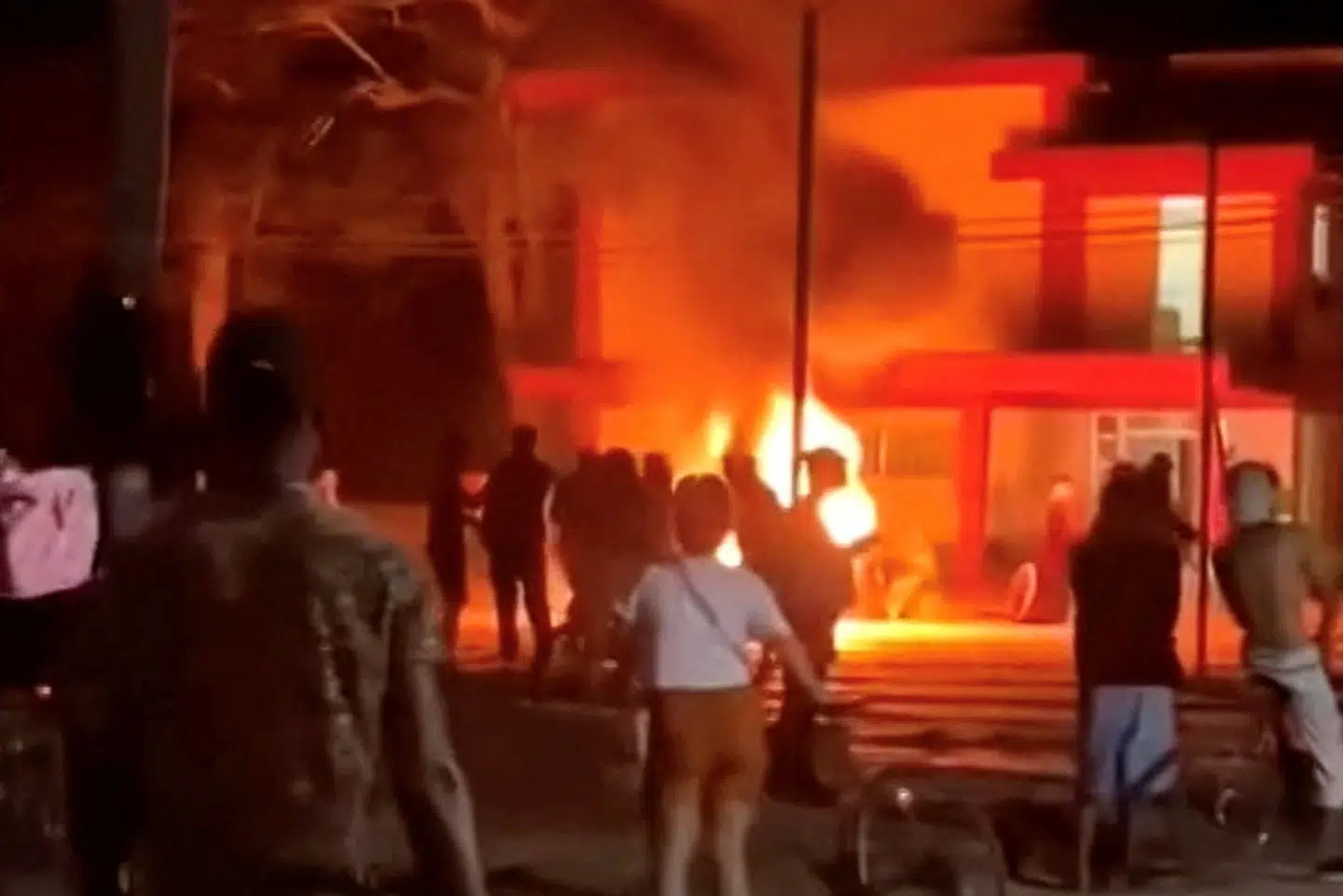 Demonstranter betragter en brændende bygning, som ifølge nyhedsbureauet Reuters' oplysninger er det cubanske kommunistpartis kontor i byen Moron i Cuba. Billedet er taget fra sociale medier.