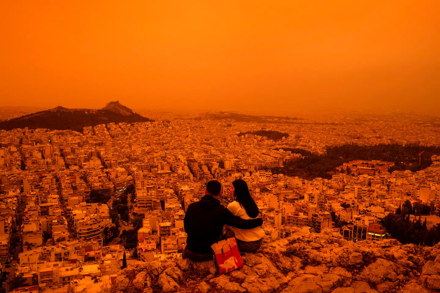 Et par nyder ekstrem orangerød solnedgang over Athen i april 2024. Forklaringen var store mængder sundhedsfarlig støv i luften fra Sahara.