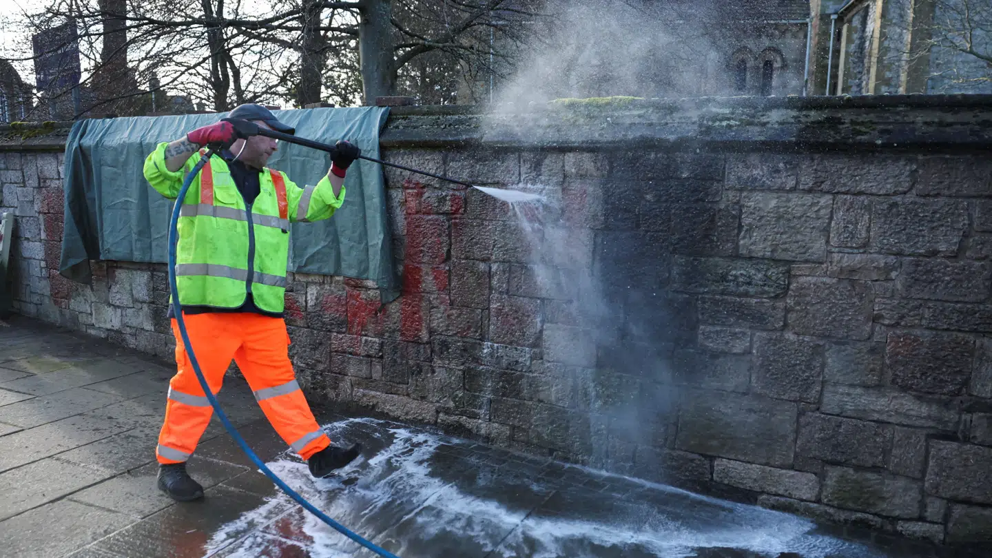 En arbejder spulede graffitien med ordene 'Not Our King' af væggen uden foran St. Asaph Katedral.