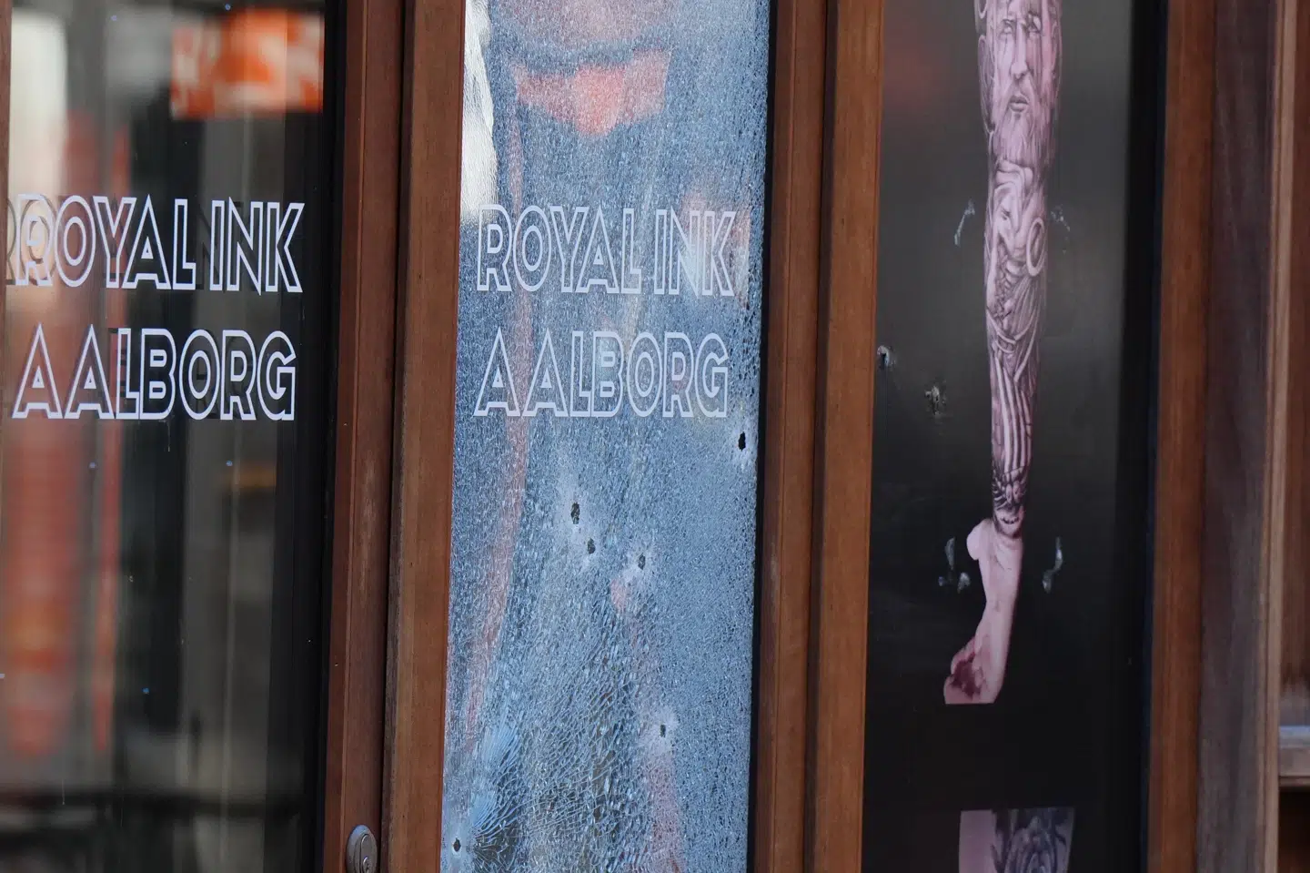 Billeder af Royal Ink i Aalborg viser seks huller i en smadret rude til tatovørforretningen. (Arkivfoto).