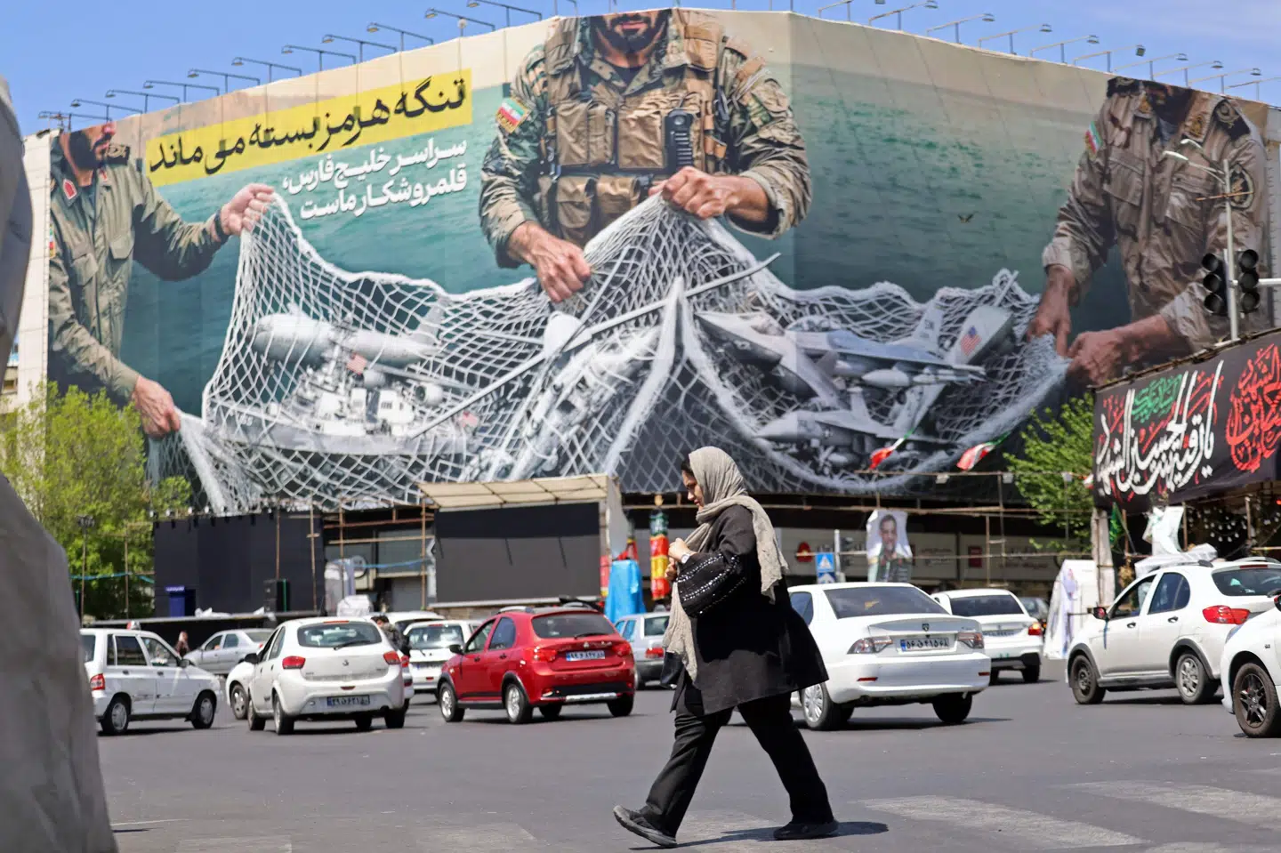 En kvinde passerer forbi et stort billboard på Revolutionspladsen i den iranske hovedstad, Teheran, søndag. Teksten lyder "Hormuzstrædet forbliver lukket". Den iranske Revolutionsgarde siger, at den har fuld kontrol med det vigtige stræde, men USA's præsident, Donald Trump, siger, at han har givet ordre til en blokade af strædet.