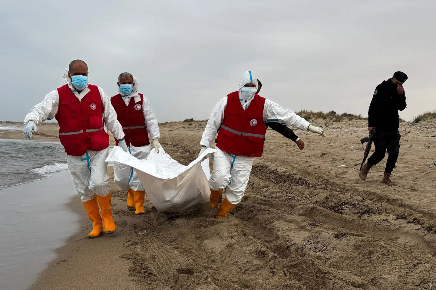 Frivillige fra hjælpeorganisationen Røde Halvmåne i Libyen bærer et lig, der er skyllet op på stranden øst for Tripoli i marts. Omkring 1000 mennesker har ifølge FN mistet livet i år i forsøget på at nå Europa via Middelhavet. (Arkivfoto).