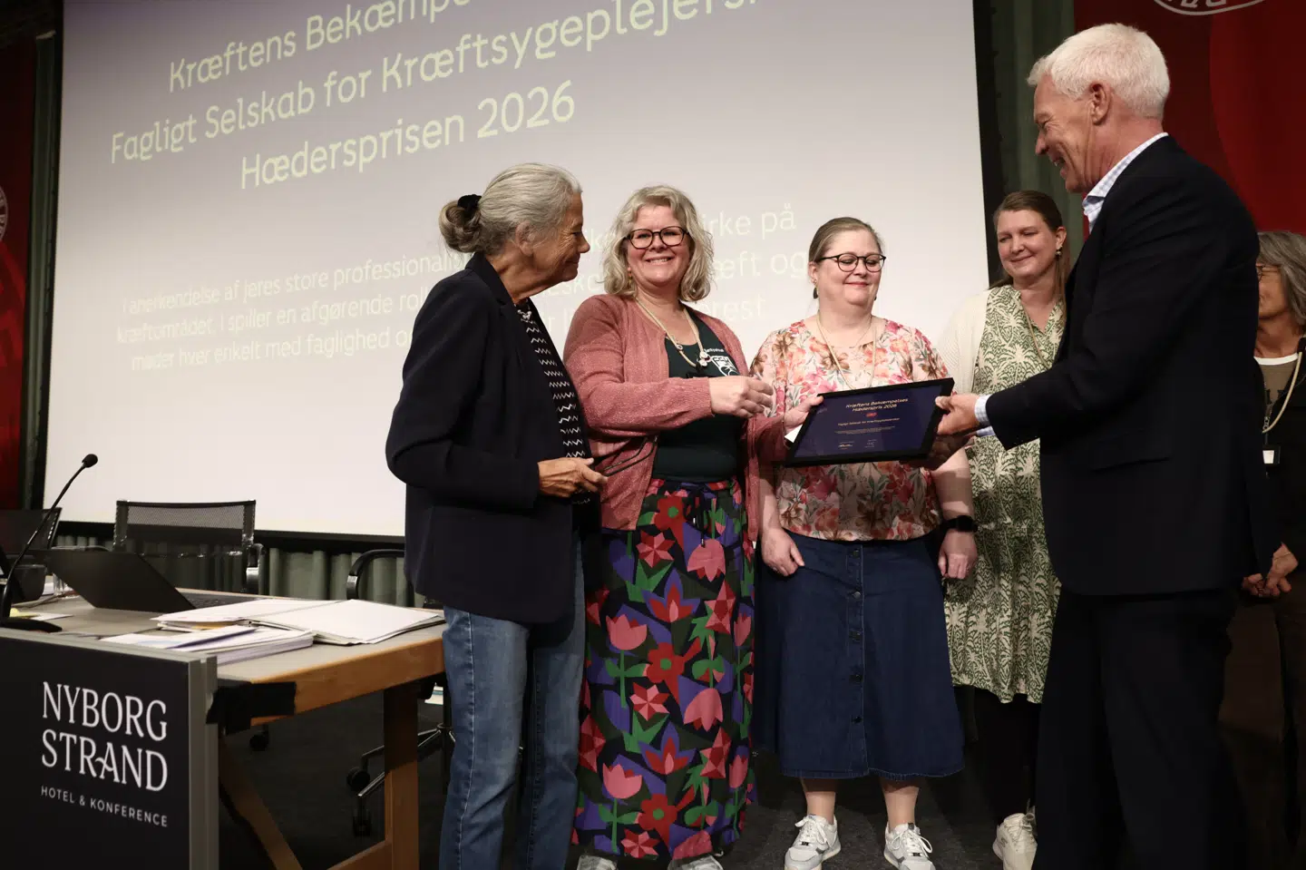 Hædersprisen 2026 blev tirsdag formiddag overrakt til landets kræftsygeplejersker ved Dansk Sygeplejeråds kongres i Nyborg. Prisen blev overrakt af formand for Kræftens Bekæmpelse Helen Bernt Andersen og direktør Jesper Fisker.