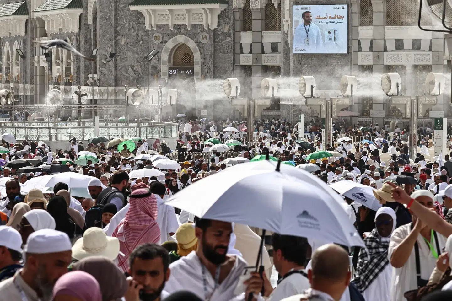 Folk dækker sig med paraplyer og går rundt under vandforstøvere for at undslippe den brændende varme i den hellige by Mekka under hajj.