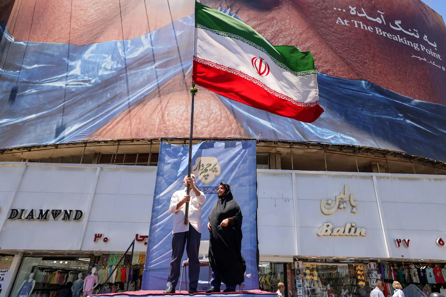 En mand står tirsdag med det iranske flag i Teheran, mens verden venter på Irans og USA's næste træk.