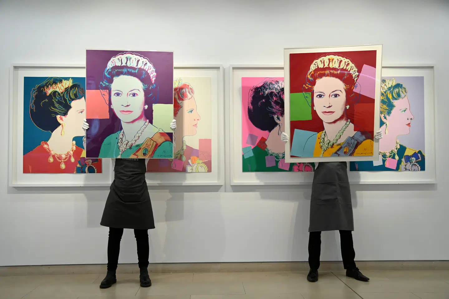 To kunstteknikere holder to portrætter af dronning Elizabeth II, som popartkunstneren Andy Warhol har skabt, op. Bag dem ses Warhols portræt af danske dronning Margrethe. To eksemplarer af værkerne kommer på auktion hos det danske auktionshus Bruun Rasmussen. (Arkivfoto).