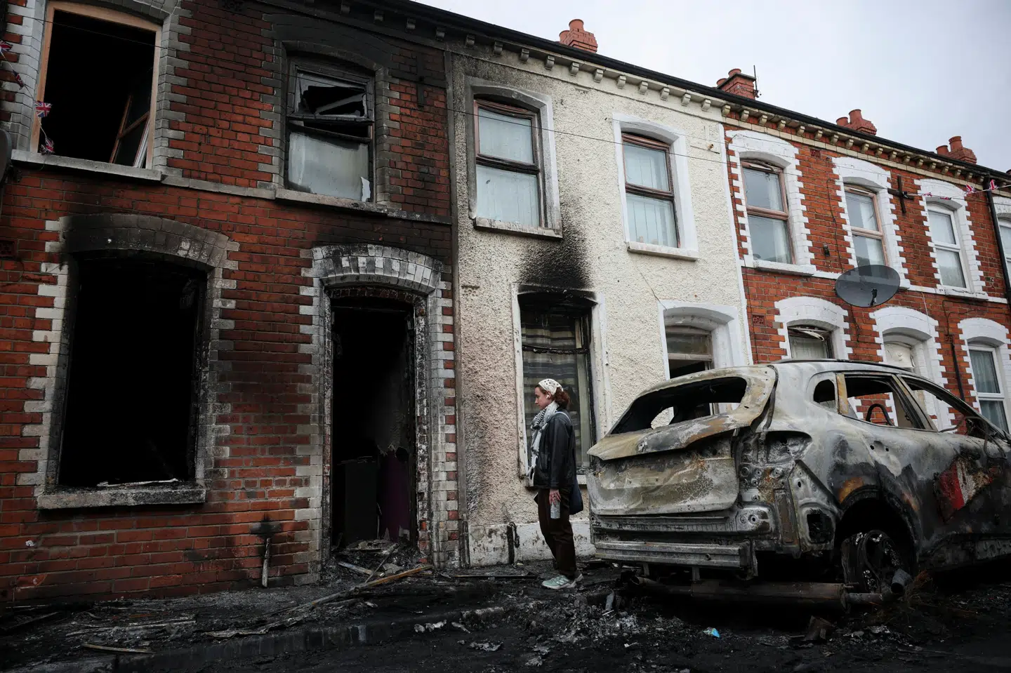 En kvinde står uden for en udbrændt hus i Belfast. Huset brød i brand i forbindelse med optøjerne tirsdag aften.