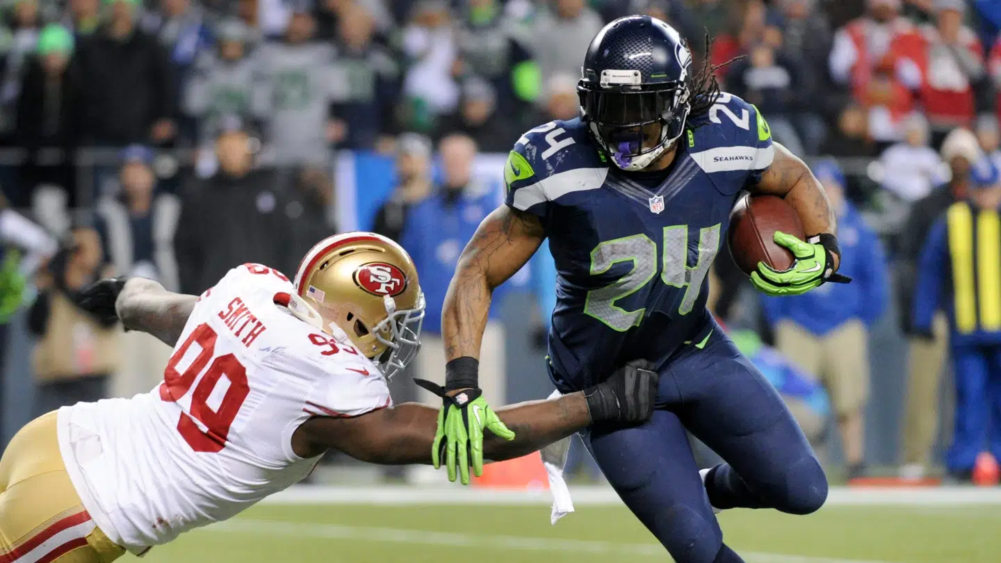 Her ses Aldon Smith (tv) under en kamp mod Seattle Seahawks i 2014. Spilleren, Smith forsøgte at tackle, er Seahawks' tidligere stjerne-runningback, Marshawn Lynch.
