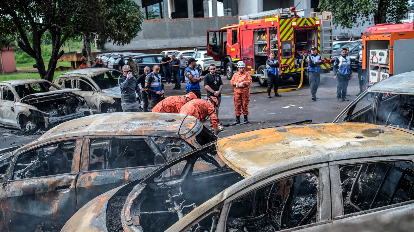 Både brandfolk og betjente arbejder ved rækken af udbrændte køretøjer efter helikopterstyrtet.