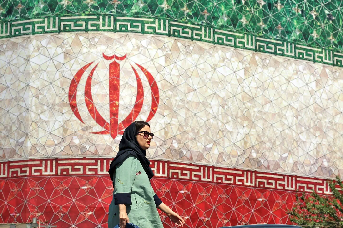 Kvinde ses foran billboard med Irans flag i landets hovedstad, Teheran, søndag. Viceudenrigsminister i landet siger sent søndag, at Iran har vundet store sejre i krigen mod USA, som der meldes at være blevet indgået aftale om. (Arkivfoto).