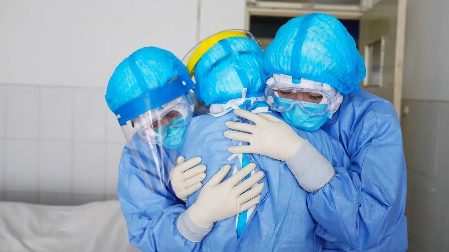 Tre sundhedsmedarbejdere iført sikkerhedsdragter krammer hinanden på en isolationsstue i et hospital i byen den kinesiske by Zouping.