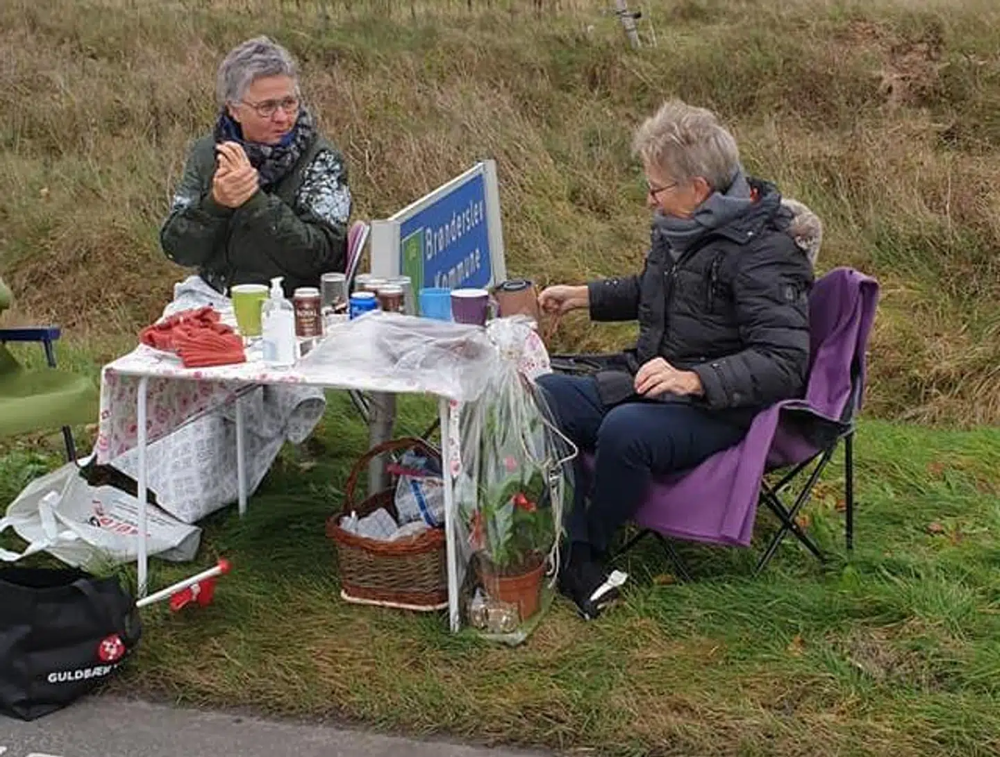 Hanne og Jette forsøger at holde varmen under strikkeklubbens møde ved Brønderslevs byskilt.