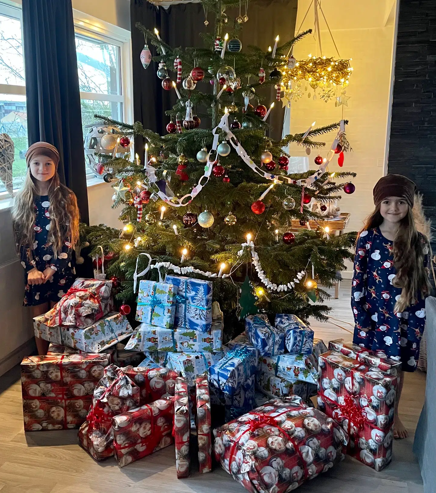 De to døtre foran det store juletræ med gaverne under.
