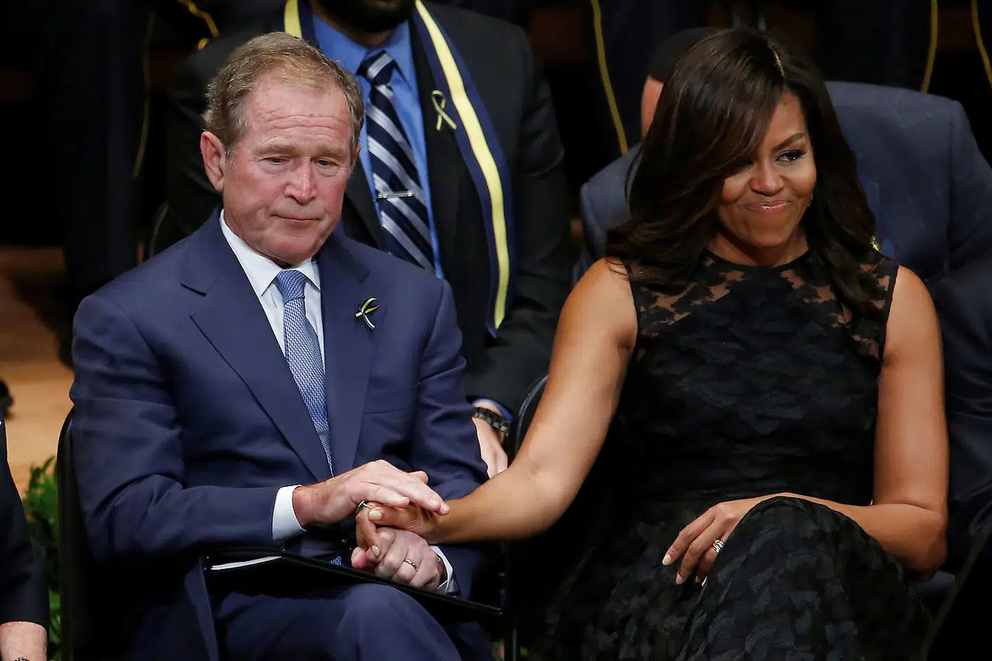 George W. Bush og Michelle Obama holder hånd under en mindeceremoni.