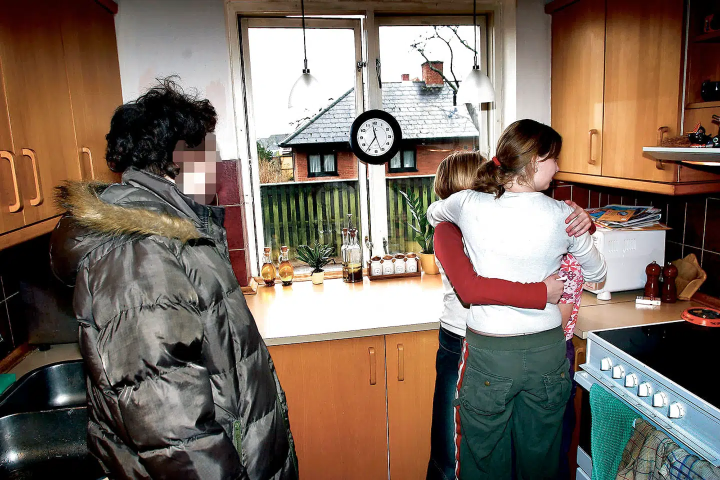 De to søskende flygtede fra deres mor (tv.) for at bo hos deres storesøster, som holder om dem i køkkenet (th.) Fotoet blev taget den dag, hvor moren, mormoren og en sagsbehandler fra kommunen kom for at tvinge pigerne tilbage til Ærø. Det lykkedes dog ikke på grund af børnenes skrig og modstand. Mandag 12. januar 2004.