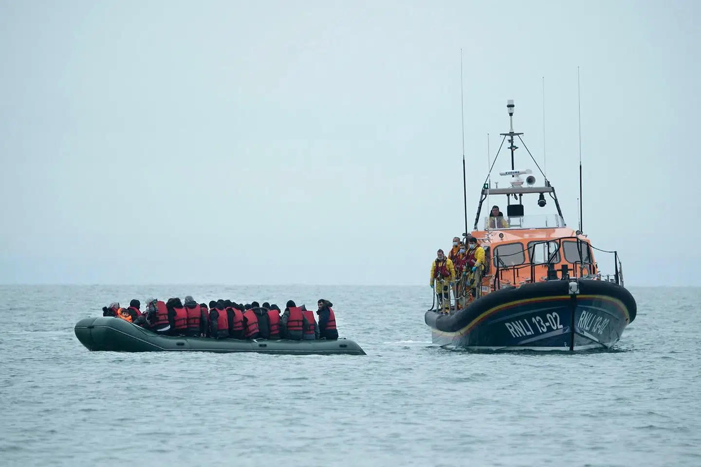 TOPSHOT - Migrants are helped by RNLI (Royal National Lifeboat Institution) lifeboat before being taken to a beach in Dungeness, on the south-east coast of England, on November 24, 2021, after crossing the English Channel. - The past three years have seen a significant rise in attempted Channel crossings by migrants, despite warnings of the dangers in the busy shipping lane between northern France and southern England, which is subject to strong currents and low temperatures. (Photo by Ben STANSALL / AFP)
