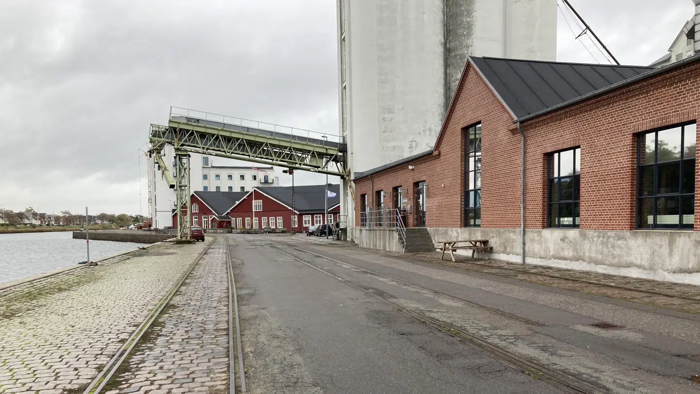 Gamle industribygninger ligger side om side med nye erhvervsbygninger, hvoraf flere er ombyggede pakhuse. Ifølge arkitekt Poul J. Larsen er det lille bord-bænkesæt et eksempel på, at man trods alt er på vej i den rigtige retninger og forsøger at skabe opholdsrum på den ellers golde kaj.